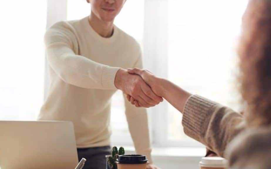 Two people shaking hands across a table. 